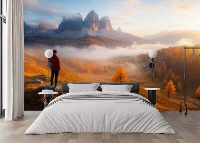 Man on stone on the hill and beautiful mountain valley in haze at colorful sunset in autumn. Dolomites, Italy. Guy, mountain ridges in fog, orange grass and trees, blue sky with sun in fall. Hiking, Wall mural