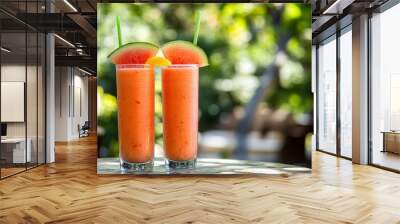 Two glasses of watermelon smoothie with watermelon and orange slices on a table in a green garden. Wall mural