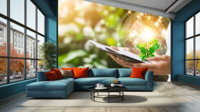 A person holds a tablet displaying a glowing plant symbolizing growth and innovation in technology and sustainability. Wall mural