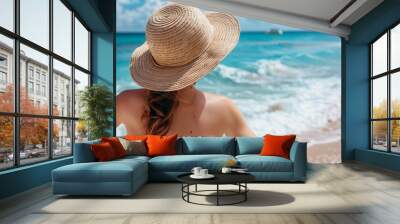 Portrait of young beautiful woman with white straw hat standing at beach. Young smiling woman on vacation enjoy sea breeze wearing straw hat and looking at camera. Attractive beautiful girl. Wall mural