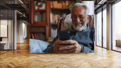 Close-up senior smiling relaxed retired man with beard and glasses sitting comfortably at home on armchair using mobile phone, communication concept Wall mural