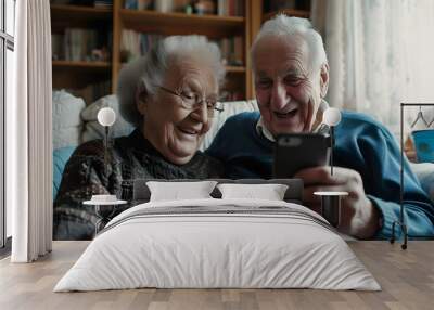 Happy smiling old pensioner couple holding a smartphone mobile phone sitting on the sofa at home, communication technology concept Wall mural