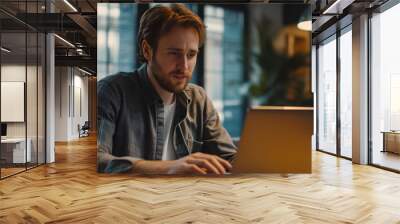 Young business man taking part in online webinar meeting looking at laptop typing sitting in an office, technology communication concept Wall mural