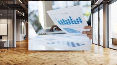 A business woman hand holding a graph and working on a laptop in the office Wall mural