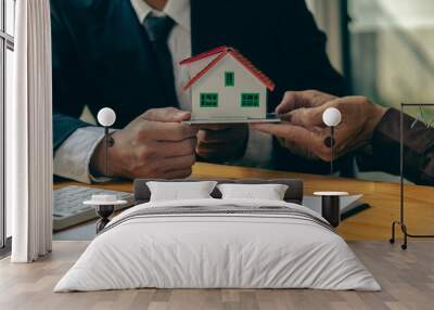 A real estate agent or bank officer explains the interest on a loan to clients with a home purchase contract and offers a title lease at the desk in the office. Wall mural