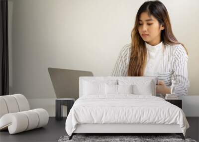 A smiling Asian businesswoman working on a laptop and holding a phone in the office sits at a desk in a financial conference room to check the accuracy of the numbers in the graph document report. fin Wall mural