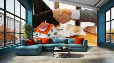 A young businessman shakes hands with a partner after Zen, a real estate investment contract document on a table with a house design and documents and money and a laptop. Wall mural