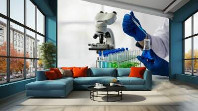 Doctor taking test tube with blue liquid, virologist working in chemical protective suit man studying dangerous virus Biologist at the lab table with a microscope in the laboratory Wall mural