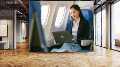 Professional Asian woman using laptop on airplane While sitting near the window in first class on an airplane during a flight travel concept Wall mural