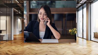 Smiling young female operator read documents and talked to clients on the mobile phone while working in his office. Wall mural