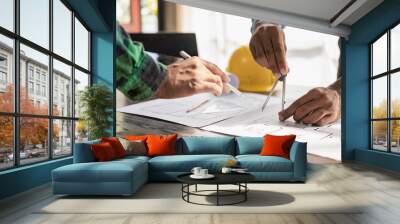 Two engineers wearing yellow clothes working and discussing white grand plan document Two colleagues discussing data and laptop with architectural project at construction site at desk in office Wall mural