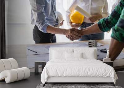 Yellow hard hat on table and house design print design with construction team handshake greeting start new project contract plan in office center at construction site partner and contractor Wall mural