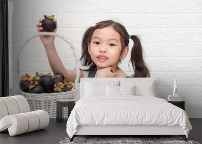 Asian little cute girl and mangosteens (Garcinia mangostana) in the wooden basket on white background. Mangosteens is a queen of fruits in thailand and very delicious. Wall mural