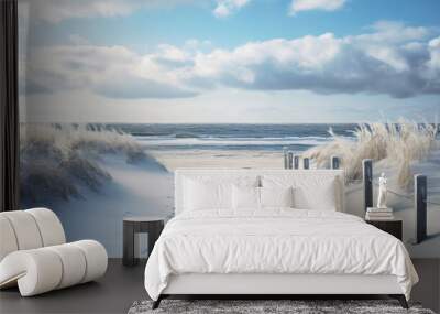 Snowy beach with evenly spaced wooden fence leading towards the ocean under a blue sky with white clouds and sand dunes covered in snow with tall grasses sticking out. Wall mural