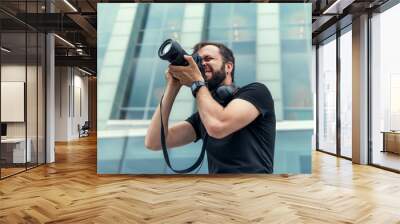 Young handsome beard man in white shirt and trousers makes beautiful pictures on film retro camera, stylishly dressed, photographer,outdoor portrait, close up,brutal, tattoo, street photo,photographer Wall mural