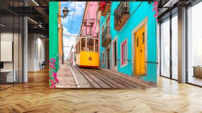 Lisbon, Portugal - Yellow tram on a street with colorful houses and flowers on the balconies - Bica Elevator going down the hill of Chiado. Wall mural