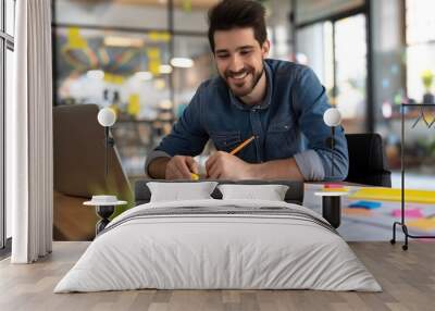 Smiling architect working on blueprints at office desk with laptop and sticky notes. Wall mural