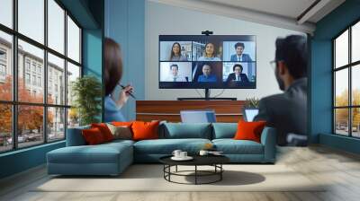 A group of individuals in an office participating in a video conference meeting, representing modern work environments, remote communication, and digital collaboration trends. Wall mural