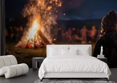 A person in warm clothing is gazing at a large bonfire during a night-time outdoor event Wall mural