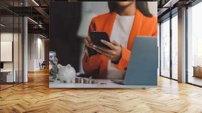 Beautiful Asian businesswoman insert coins in a pin piggy bank on the table. saving money, investment, currency concept Wall mural