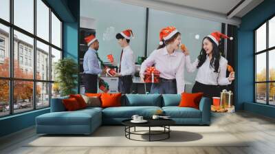 full length view of a group of business team wearing red Santa hat and exchange gift box together in the office for Christmas. Wall mural