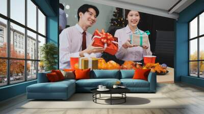 full length view of a group of business team wearing red Santa hat and exchange gift box together in the office for Christmas. Wall mural