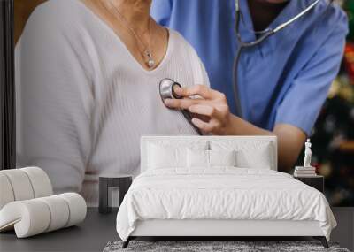 Homecare nursing service and elderly people cardiology healthcare. Close up of young hispanic female doctor nurse check mature caucasian man patient heartbeat using stethoscope during visit Wall mural