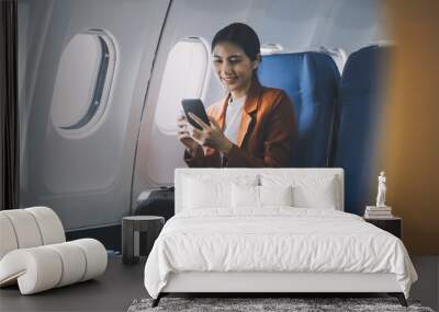 Traveling and technology. Flying at first class. Pretty young businees woman using smartphone while sitting in airplane. Wall mural