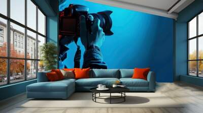 A photographer in a blue jacket holds a camera with a lens cap, taking a photo. Wall mural