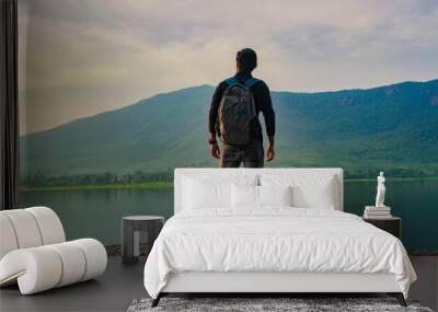 Young man standing near the lake and mountain and enjoying the view of nature Wall mural