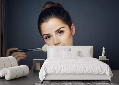 Looking fresh by adding some blush. Studio shot of a beautiful young woman applying blush on her cheeks while posing against a blue background. Wall mural