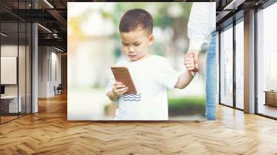 Little boy concentrate at smartphone with his mom holding his hand. Wall mural