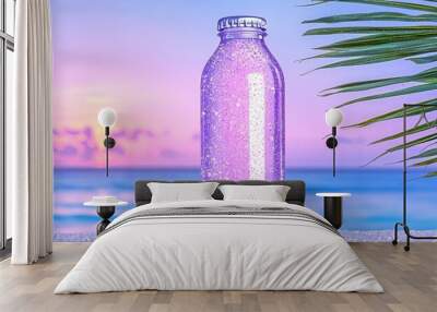 Purple glass bottle on sandy beach with palm and sunset in background. Wall mural