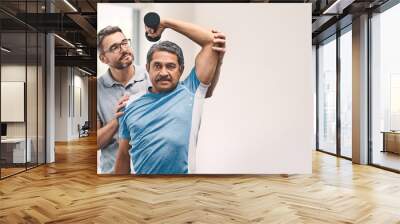 Proper technique is the main focus. Shot of a senior man exercising with dumbbells during a rehabilitation session with his physiotherapist. Wall mural