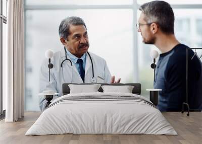 Hes explaining all the steps that need to be taken. Shot of a confident mature male doctor consulting a patient inside a hospit. Wall mural