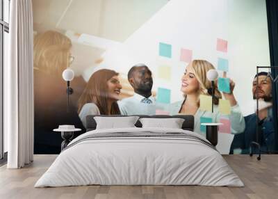 Marketers flexing their mental muscles. Shot of a group of businesspeople arranging sticky notes on a glass wall in a modern office. Wall mural