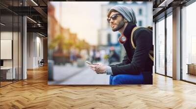 Miles away in the middle of it all. Shot of a young man using his mobile phone while out in the city. Wall mural