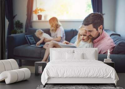 They keep their home connected. Shot of an adorable little girl using a digital tablet with her father on the sofa at home. Wall mural