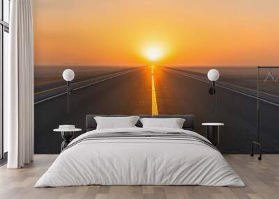 A serene road stretching towards a vibrant sunset, illuminating the horizon with warm golden hues. Wall mural