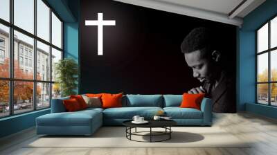 African man in suit is praying and giving thanks to god in dark room with crucifix Wall mural