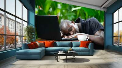 African man sleeping on laptop with green nature background. Wall mural