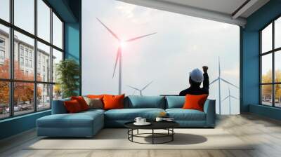 Successful engineer standing and hoding labtop with wind turbine. Wall mural