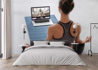 Close up of young sporty woman practicing yoga online with laptop at home. Yoga instructor conducting video training via video conference. Meditation, Sukhasana, relax. Healthy lifestyle concept Wall mural