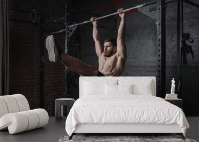 Crossfit athlete doing abs exercises on horizontal bar. Practicing calisthenics at gym. Wall mural