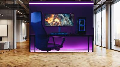 General view of home workplace of pro gamer with professional gaming setup on desktop. Modern powerful PC full RGB light inside, display with shooter game, armchair. Gaming studio of cyber sportsman Wall mural