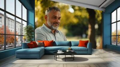 Middle-aged man in casual attire on a park bench, engaged in conversation with a woman, trees and greenery in the background, bright outdoor light Wall mural