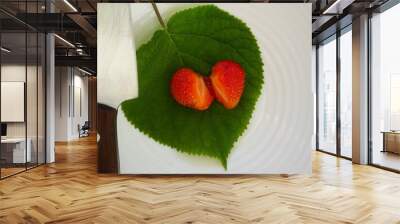 Red strawberry in the shape of a heart, cut in half with a knife, on a green wooden leaf Wall mural