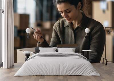 a young woman in a warehouse setting, carefully labeling or writing on a cardboard box, businesswoman, small business owner holding pen writing addressee details on cardboard box Wall mural