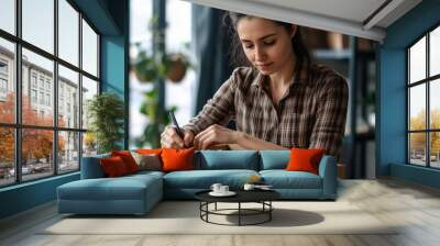 a young woman in a warehouse setting, carefully labeling or writing on a cardboard box, businesswoman, small business owner holding pen writing addressee details on cardboard box Wall mural