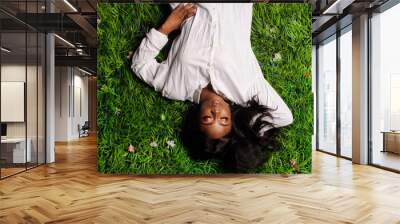 Portrait of beautiful african american woman laying on green grass in park Wall mural